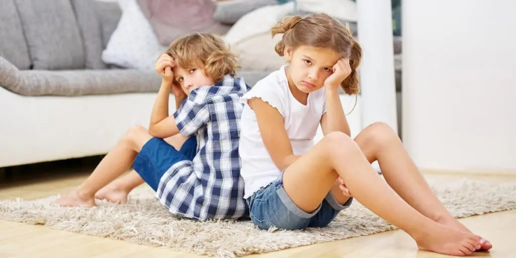 Two unhappy children sitting back to back, emphasizing the importance of following these tips for divorcing parents